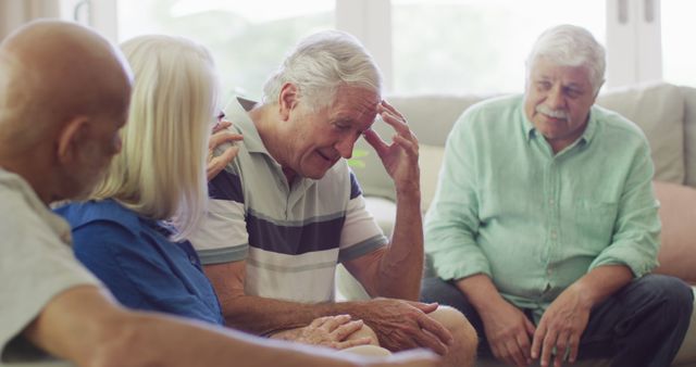 Group of elderly people supporting a man who appears distressed. Others around him are comforting and engaging him. Suitable for use in articles and media focused on elderly care, mental health, emotional support, senior living communities, and family support for senior citizens.