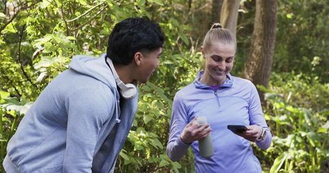 Pair pausing on forest trail during workout, checking phone and hydrating