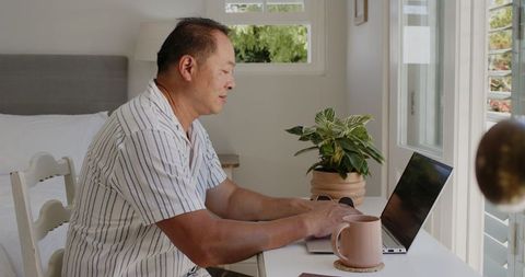Senior Man Enjoying Morning Coffee While Working on Laptop at Home