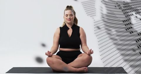 Curvy woman meditating in lotus pose on black yoga mat with minimalist monochrome panel