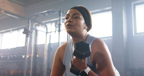 Focused african american woman lifting dumbbell in industrial gym for strength training