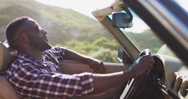 African american man with hands on steering wheel sitting in the convertible car on road. road trip travel and adventure concept