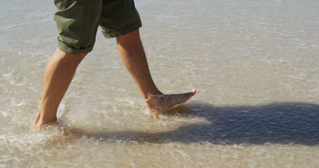 A person is walking through shallow water at the beach, with copy space. Bare feet stepping into the sea evoke a sense of relaxation and connection with nature.