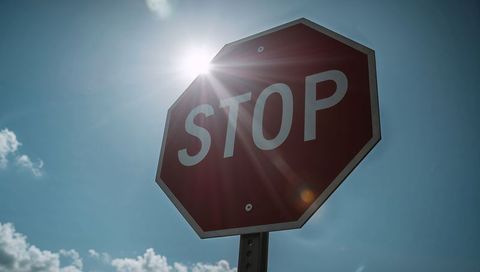 Sun flare streaking across red octagon stop sign with lens flare and bright blue sky
