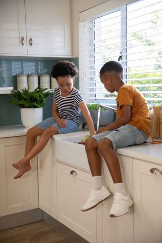Diverse siblings chatting on kitchen countertop with farmhouse sink