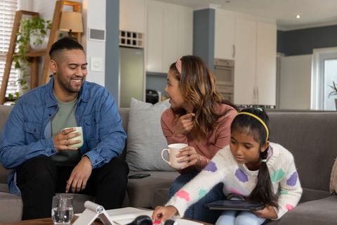 Modern family relaxing on sofa with child using tablet while parents enjoying coffee
