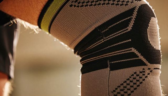 Rim-lit knee wearing compression sleeve with geometric knit and neon trim for workout