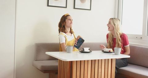 Friends sharing coffee and cake in sunlit minimalist kitchen nook, cozy banquette moment