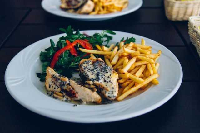 This photo shows a delicious and balanced meal served on a white plate. Grilled chicken breast is accompanied by fresh vegetables, including leafy greens and bell peppers, and a side of crispy French fries. Perfect for use in food blogs, recipe websites, restaurant menus, or any content promoting healthy eating. The combination of proteins, greens, and crispy fries highlights a nice and inviting meal.