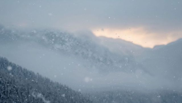 Snow Falling Over Misty Alpine Ridge with Pale Sunrise Glow
