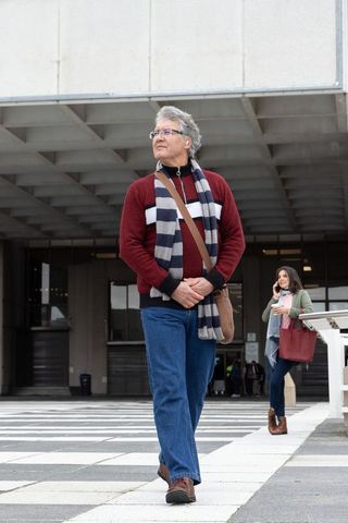 Senior man walking through urban plaza with striped scarf and messenger bag, commuting