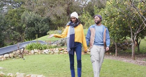 Couple walking hand in hand through residential garden wearing knit beanies and scarves