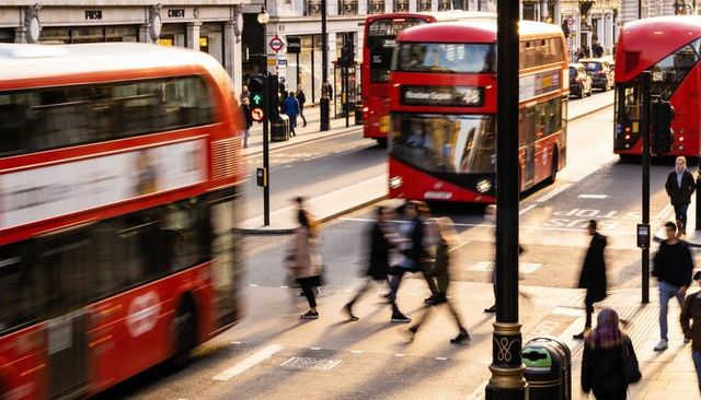 London commuters hurrying across zebra crossing beside red double-decker buses at sunset