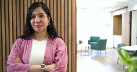 Confident professional woman standing with arms crossed in modern office lounge interior