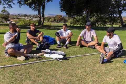 Young men relaxing after practice on sunlit sports field, team bonding and gear