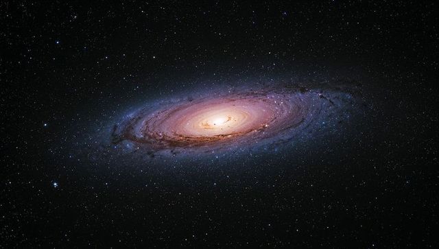 Spiral galaxy tilting and glowing with luminous core and dark dust lanes