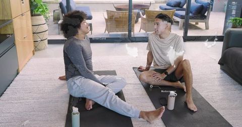 Two men stretching and chatting on yoga mats in modern living room for fitness lifestyle