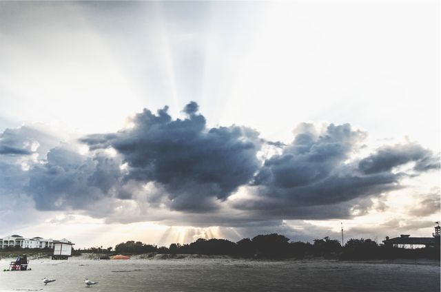 Dramatic sun rays are breaking through clouds over the coastal beach, creating a striking and tranquil scene. Perfect for use in travel promotions, inspirational blogs, weather-related content, and meditation visuals. This scenery evokes a sense of calm and natural beauty.