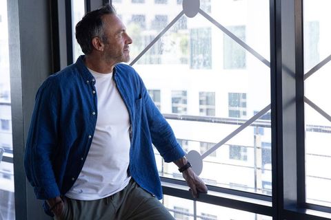 Mature man leaning at office window checking wristwatch, contemplative urban professional