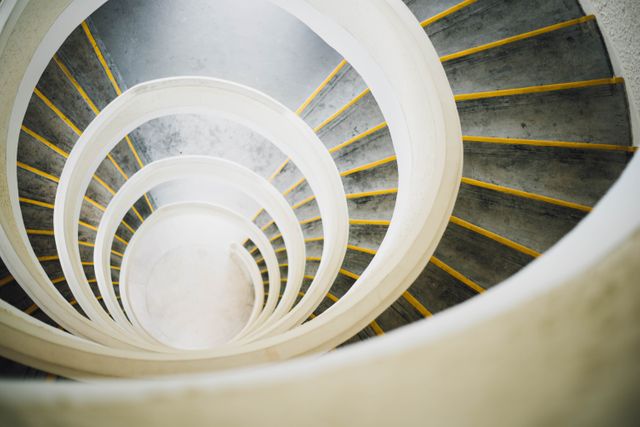 Top view of a spiral staircase showing yellow-edged steps. Symmetrical and geometrically appealing, ideal for use in architectural magazines, design blogs, or modern art exhibits. Great for highlighting concepts of infinite loops or modern interior design.