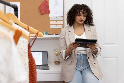 African american fashion designer working on tablet in design studio with clothing rack