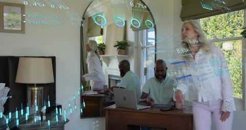Senior woman walking as man working on laptop with holographic finance data at home serene