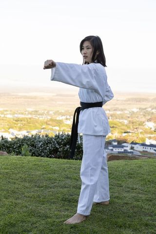 Asian woman practicing karate forward punch outdoors in nature