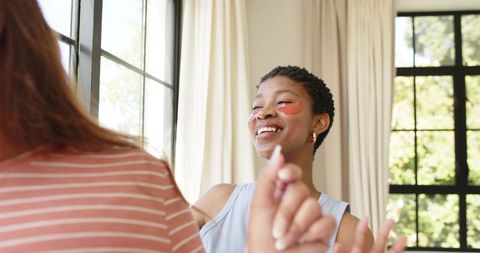 Joyful african american women applying under-eye gel patches during home skincare self-care