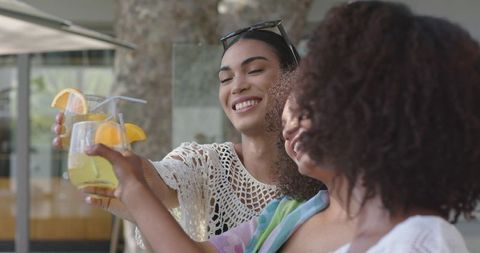 African american friends toasting citrus cocktails on sunny patio, smiling together