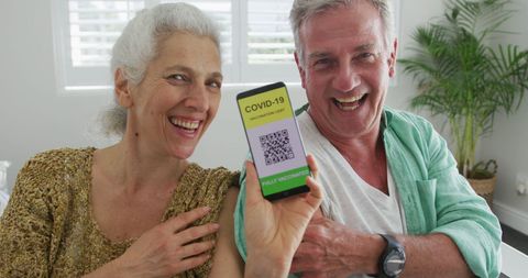 Happy senior couple celebrating covid-19 vaccination with digital passport