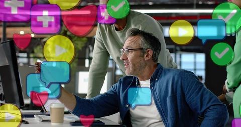 Middle-aged man pointing at monitor, collaborating with team, floating social media icons