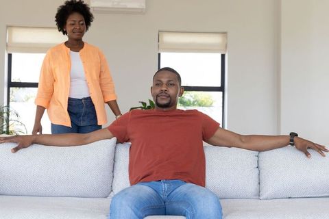 African american couple relaxing on minimalist sofa in bright neutral living room