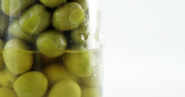 Close-up view of green peas preserved in a jar, with copy space on the right side. The image captures the detail of the peas and the bubbles trapped in the liquid, emphasizing the preservation process.