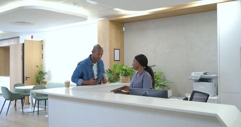 African american man speaking with receptionist at modern medical office reception desk