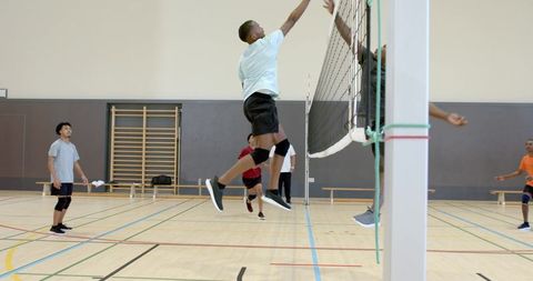 Young men playing indoor volleyball jumping to spike and block on wood court