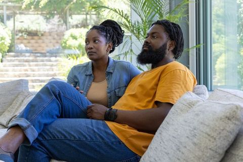 African american couple relaxing on sofa by glass window with garden view, cozy lifestyle