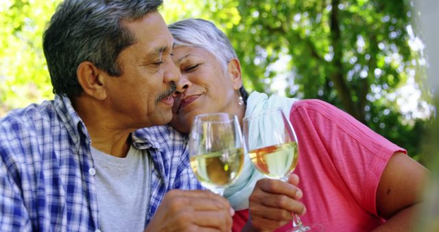A middle-aged couple enjoys a romantic moment outdoors, toasting with glasses of wine, with copy space. Their affectionate embrace and content smiles evoke a sense of love and companionship.