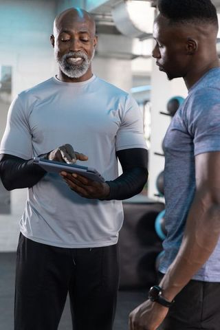 Senior african american trainer showing digital workout plan on tablet to male trainee