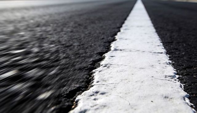 Ground-level worn white lane line leading to horizon, textured asphalt with motion blur