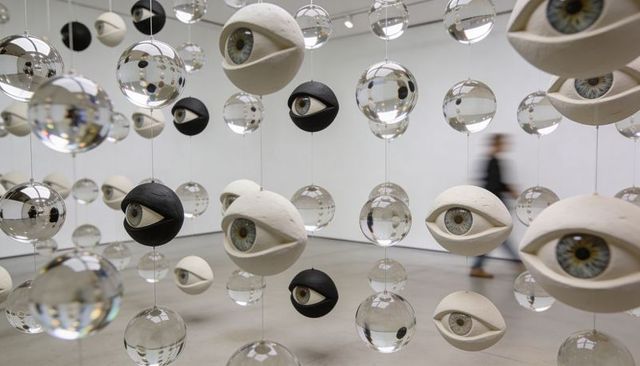 Hanging eye orb installation in modern gallery with mirrored spheres and blurred visitor