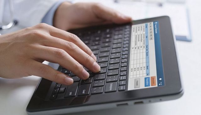 Doctor typing patient records on tablet keyboard stethoscope white coat cuff clinical closeup