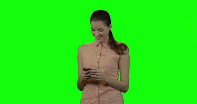 Young woman wearing casual clothing, smiling and texting on her smartphone against a green screen background. Perfect for marketing communications, technology apps, and website designs.