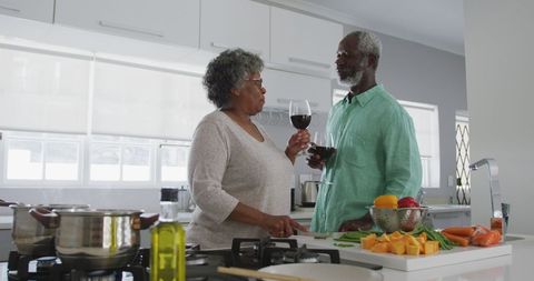 scene capturing a senior couple enjoying each other's company while sipping wine in a contemporary kitchen. they share a warm moment during meal preparation, highlighting comfort and intimacy in a familiar home environment. ideal for use in lifestyle promotions, cooking content, and advertisements focused on senior living, family life, or culinary enjoyment.