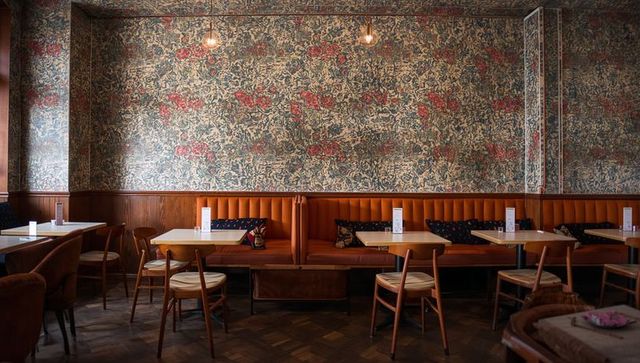 Cozy vintage cafe interior featuring tufted burnt-orange banquette and floral wallpaper