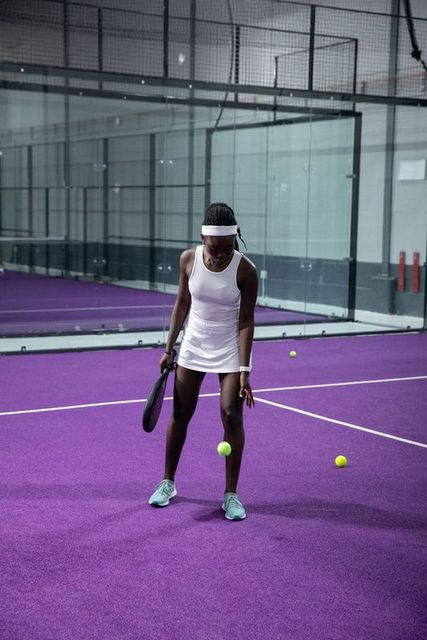 African american woman practicing padel on purple indoor court bouncing ball with racket