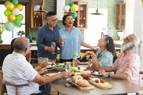 Multicultural friends celebrating at home dinner party with wine and laughter