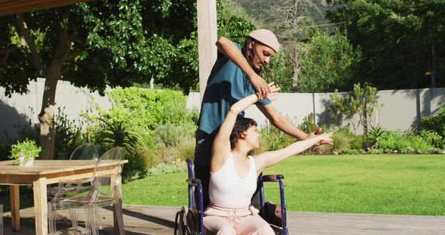 Happy biracial couple dancing on terrace in garden, woman in wheelchair, man with dreadlocks. wellbeing and domestic lifestyle with physical disability.