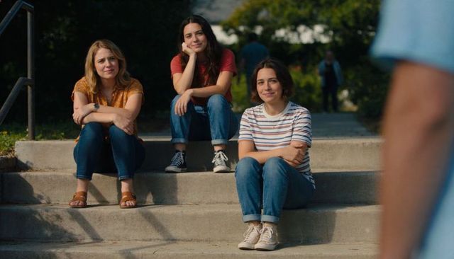 Three young women sitting on campus steps chatting and laughing in casual jeans