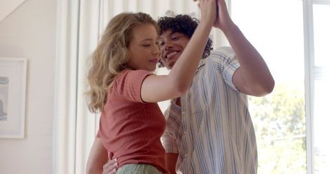 Couple dancing in cozy living room with white curtains