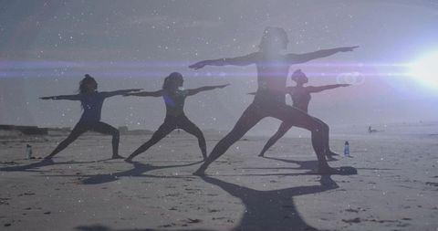 Sunlit beach yoga class practicing warrior poses silhouettes with instructor and group